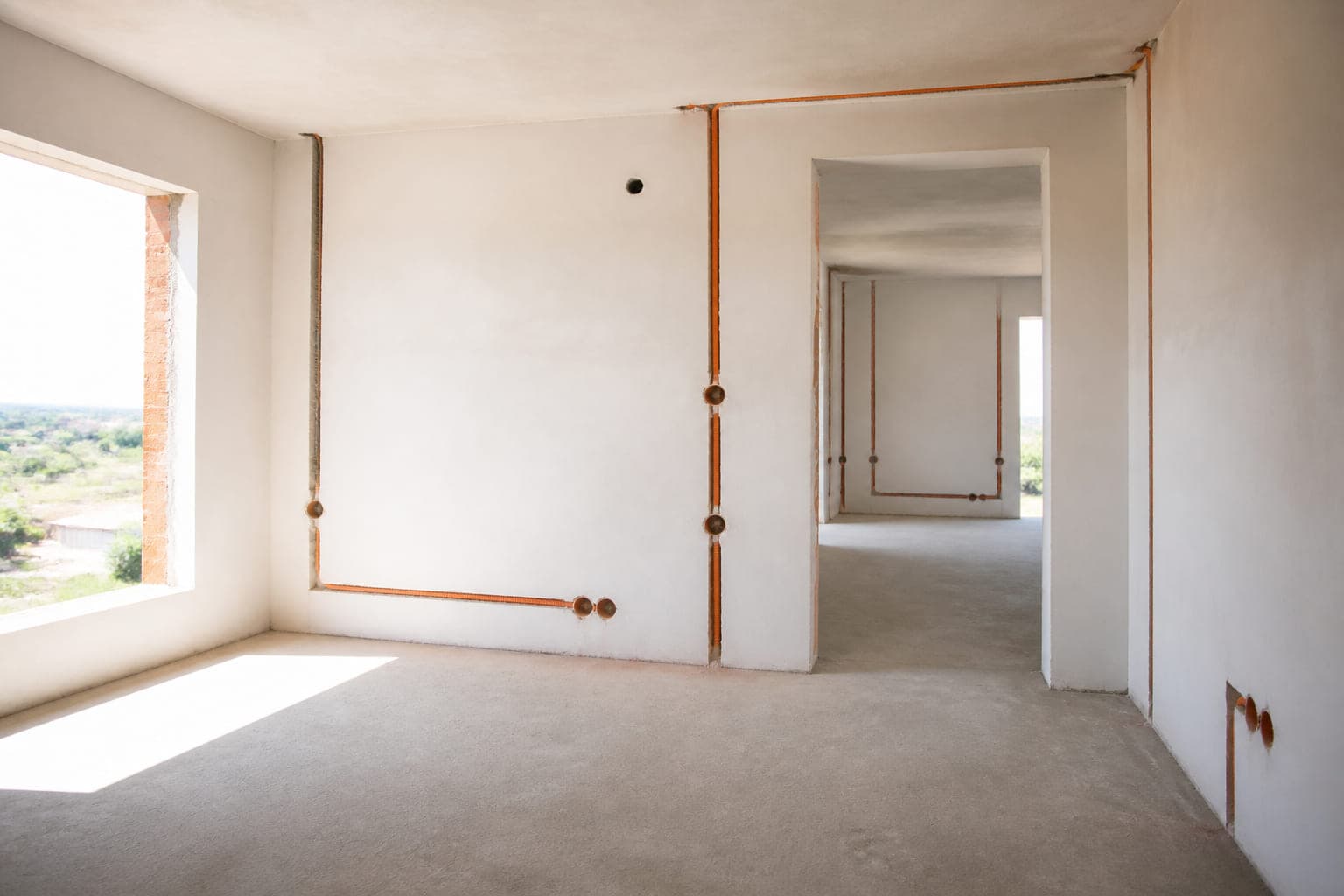Heller Rohbau mit orangen Leerrohren in gefrästen Wandschlitzen und großen Fensteröffnungen
